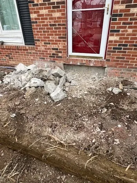 Construction site: stones and dirt in front of a brick building entrance with a red door.