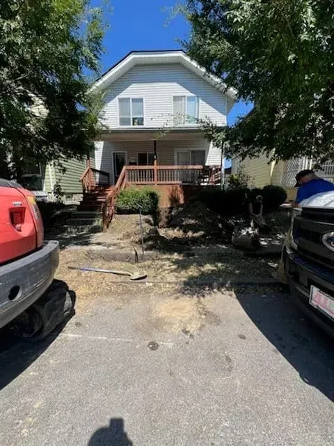 A two-story white house with a porch, landscaping, and a red construction vehicle.
