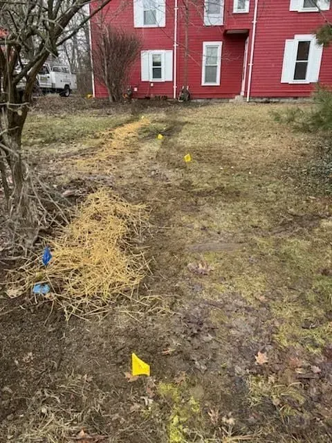 Muddy yard with yellow flags marking underground lines in front of a red building.