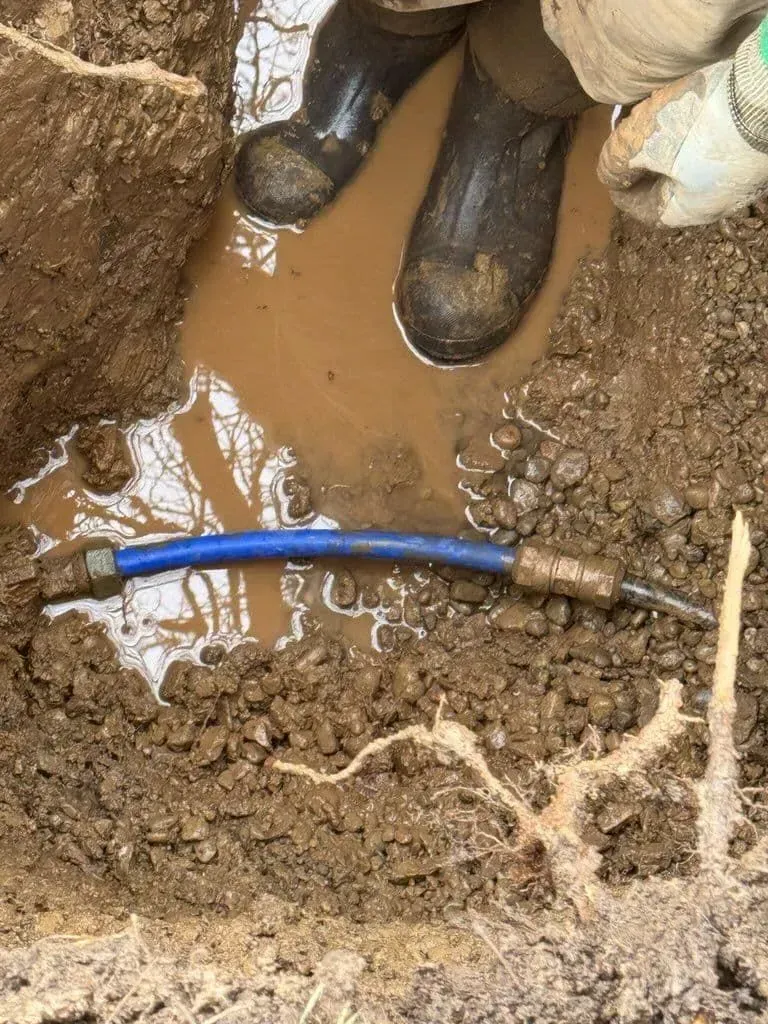 Person in boots standing in muddy water with a blue pipe visible.