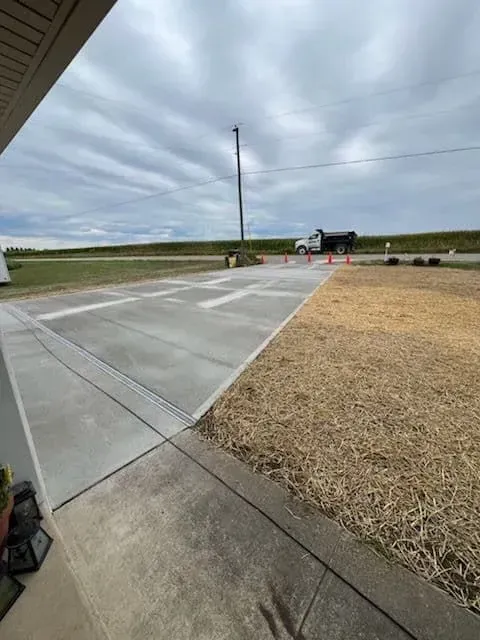 New concrete driveway next to dry grass; cloudy sky and truck in the background.
