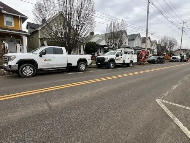 White utility trucks parked along a street in front of houses; cloudy sky overhead.