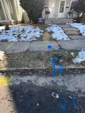 Sidewalk with utility markings and snow patches in front of a house. Blue and yellow paint marks.