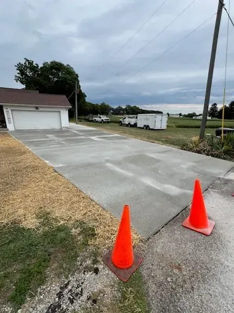 Newly poured concrete driveway with orange safety cones, leading to a garage. Overcast sky.