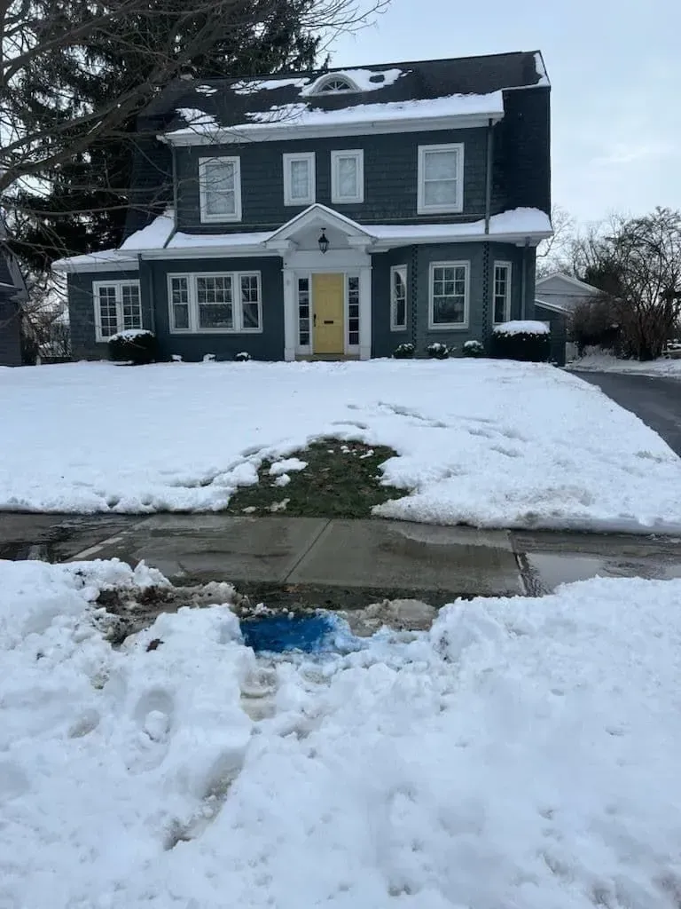 Two-story house with dark gray siding, yellow door, and snow-covered lawn.