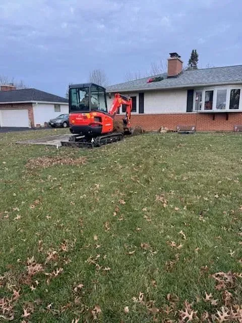 Orange excavator digging near a house with a brick facade.
