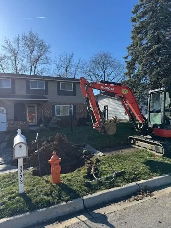 An orange Kubota excavator digging in a residential yard near a fire hydrant and mailbox on a sunny day.