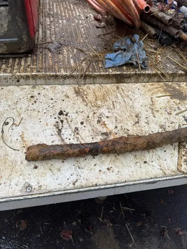 Rusty metal pipe on a dirty white surface with copper tubes in the background.