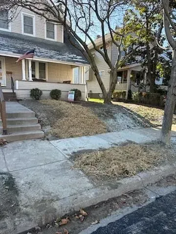 Trench in brown soil with exposed pipes, a shovel, and a white pipe near a building.