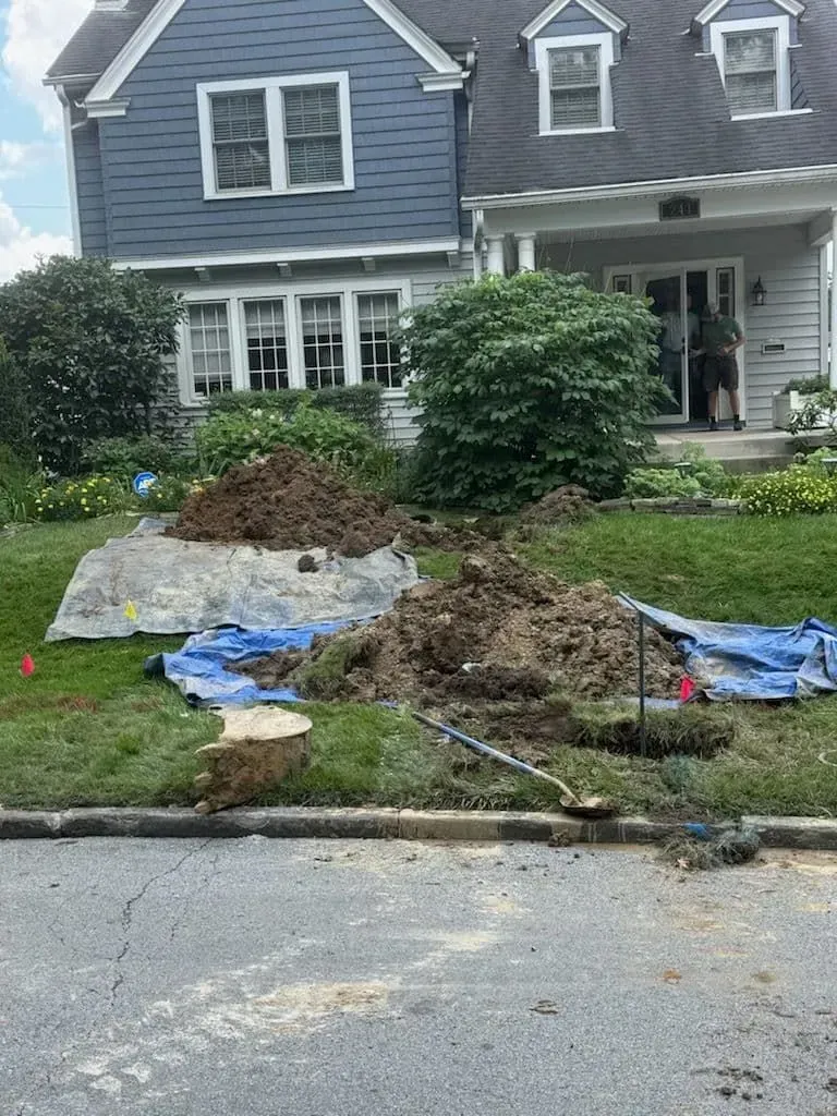Yard excavation with piles of dirt on a tarp in front of a blue and white house. A person stands in the doorway.