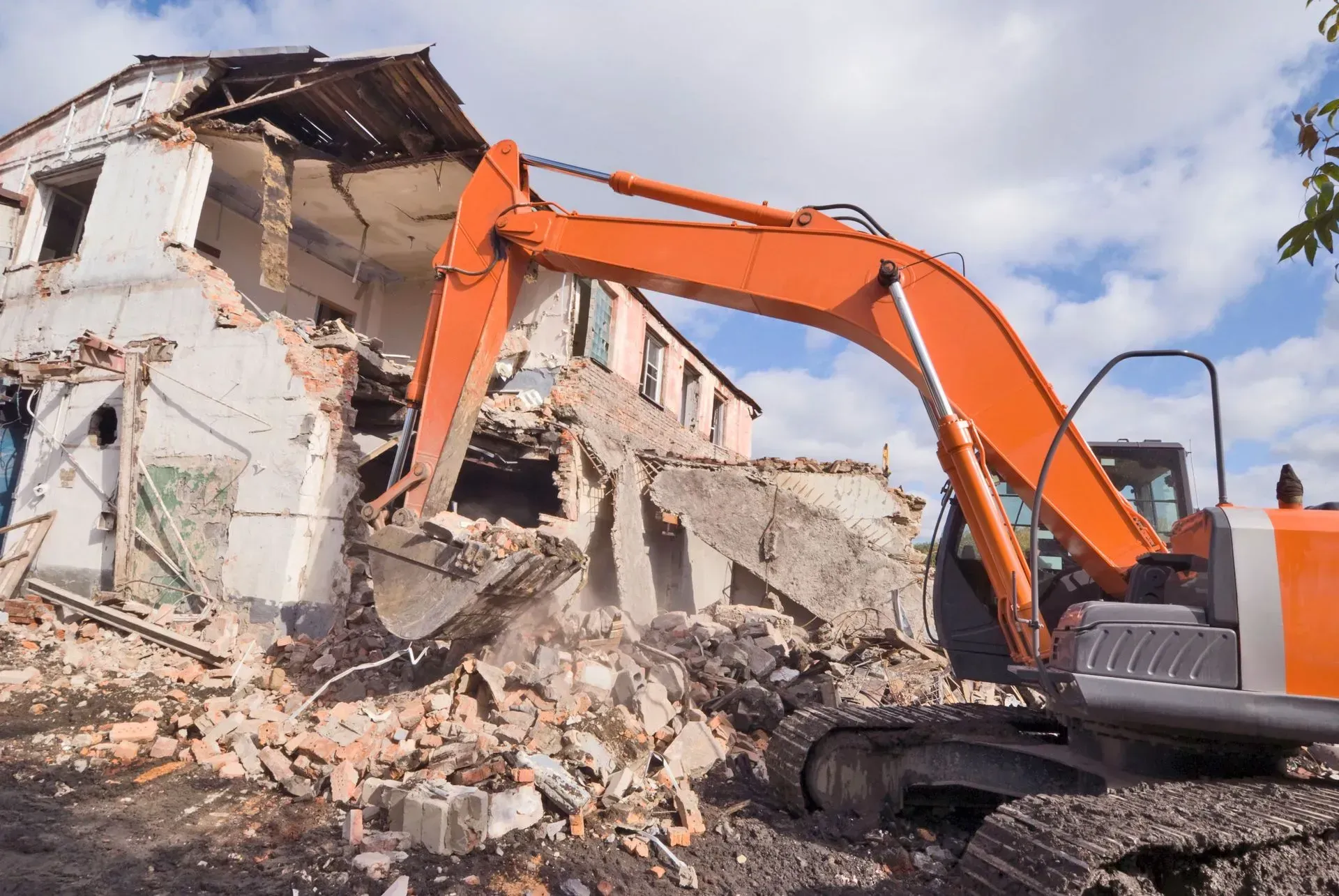 Orange excavator demolishing a building; rubble, daylight.