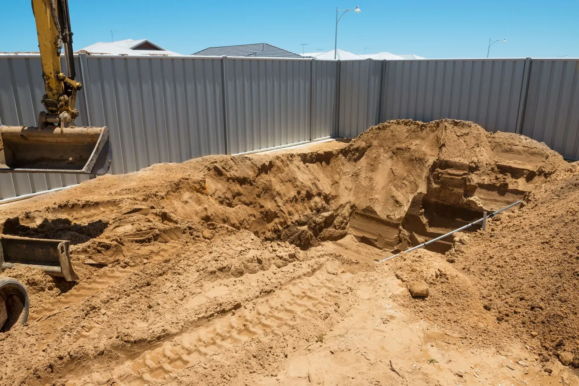 Excavator digging a rectangular pool foundation in red soil, wooden framework around perimeter.
