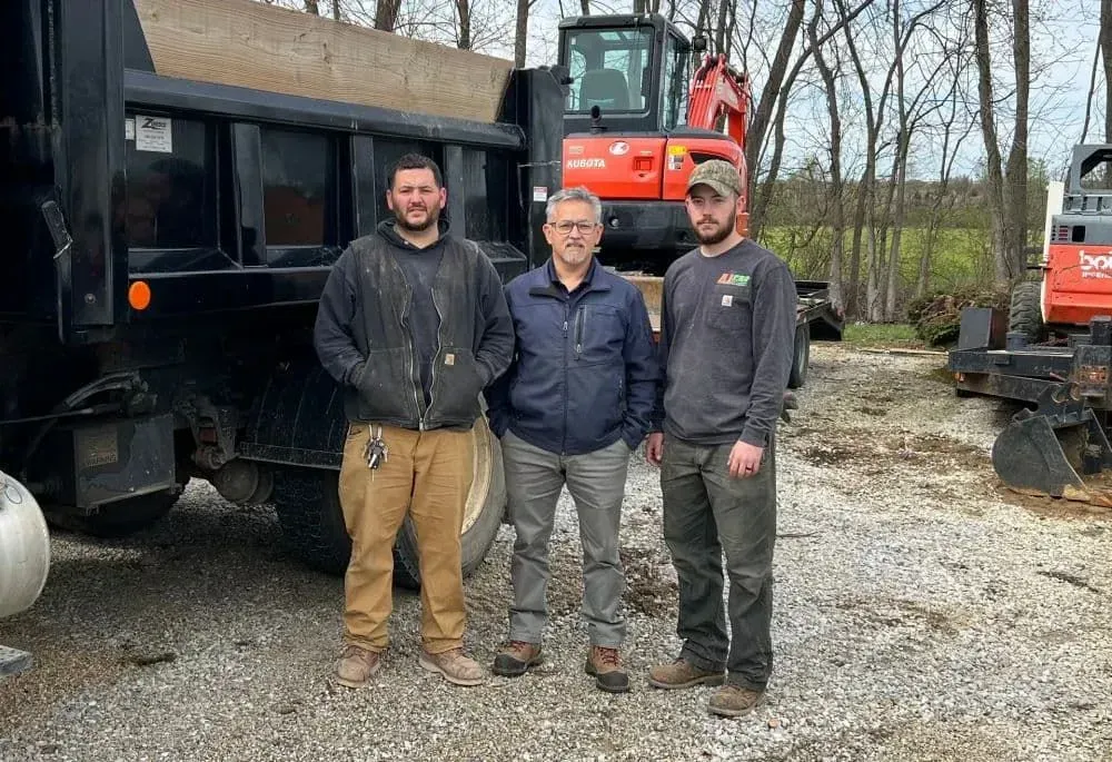 A rectangular hole dug next to a building's foundation; dirt walls. Tools and trash cans in the background.