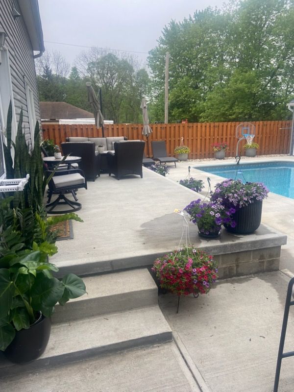 A rectangular pool with light blue water and a concrete deck; two houses and trees in the background.