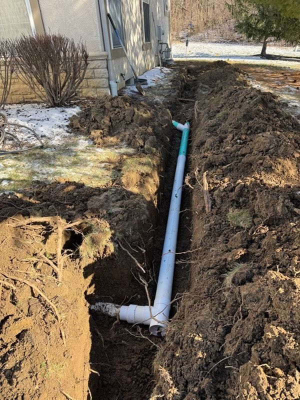 Trench with exposed red pipe elbow connected to a blue water pump. Soil, a yellow tool, and a concrete surface.