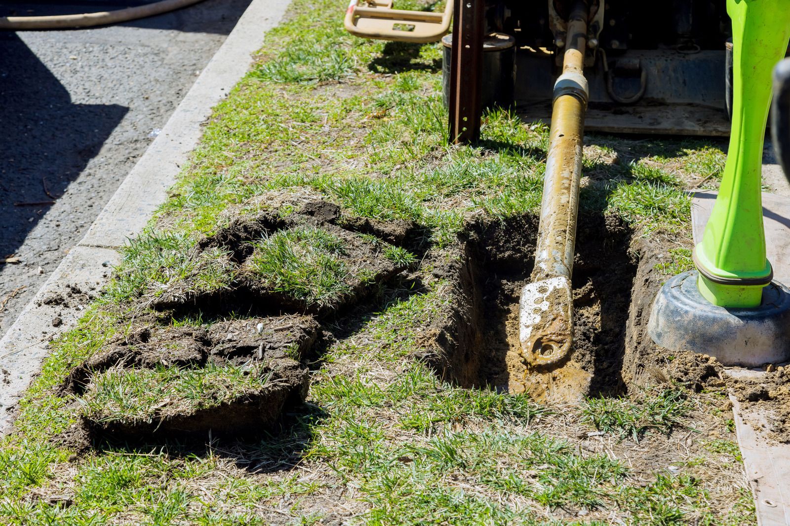 A rectangular hole dug next to a building's foundation; dirt walls. Tools and trash cans in the background.