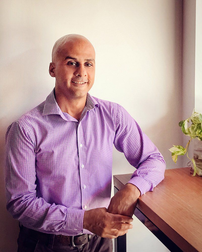 A man in a purple shirt is leaning on a wooden table.