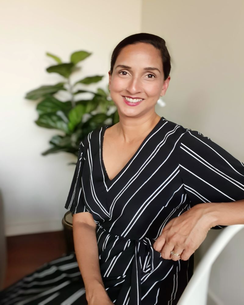 A woman in a black and white striped dress is leaning on a white chair.