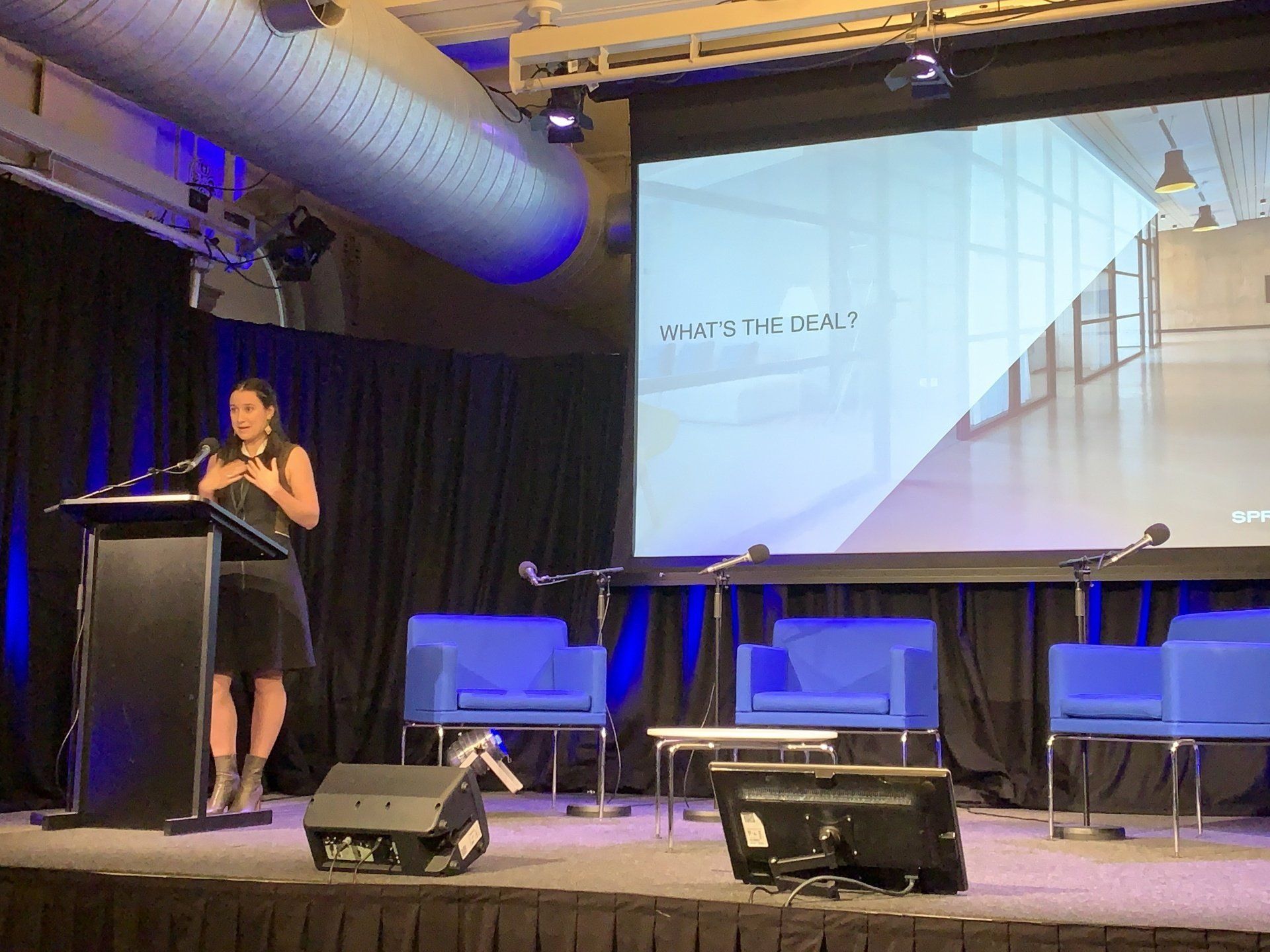 A woman is standing at a podium giving a presentation in front of a large screen.