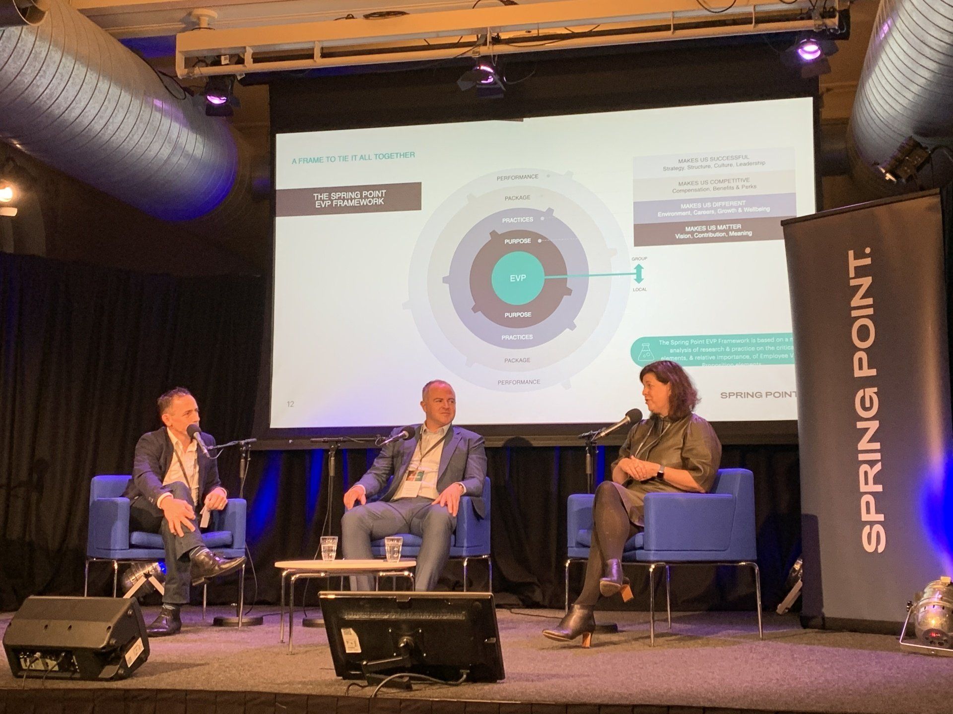 A group of people are sitting on a stage in front of a large screen.