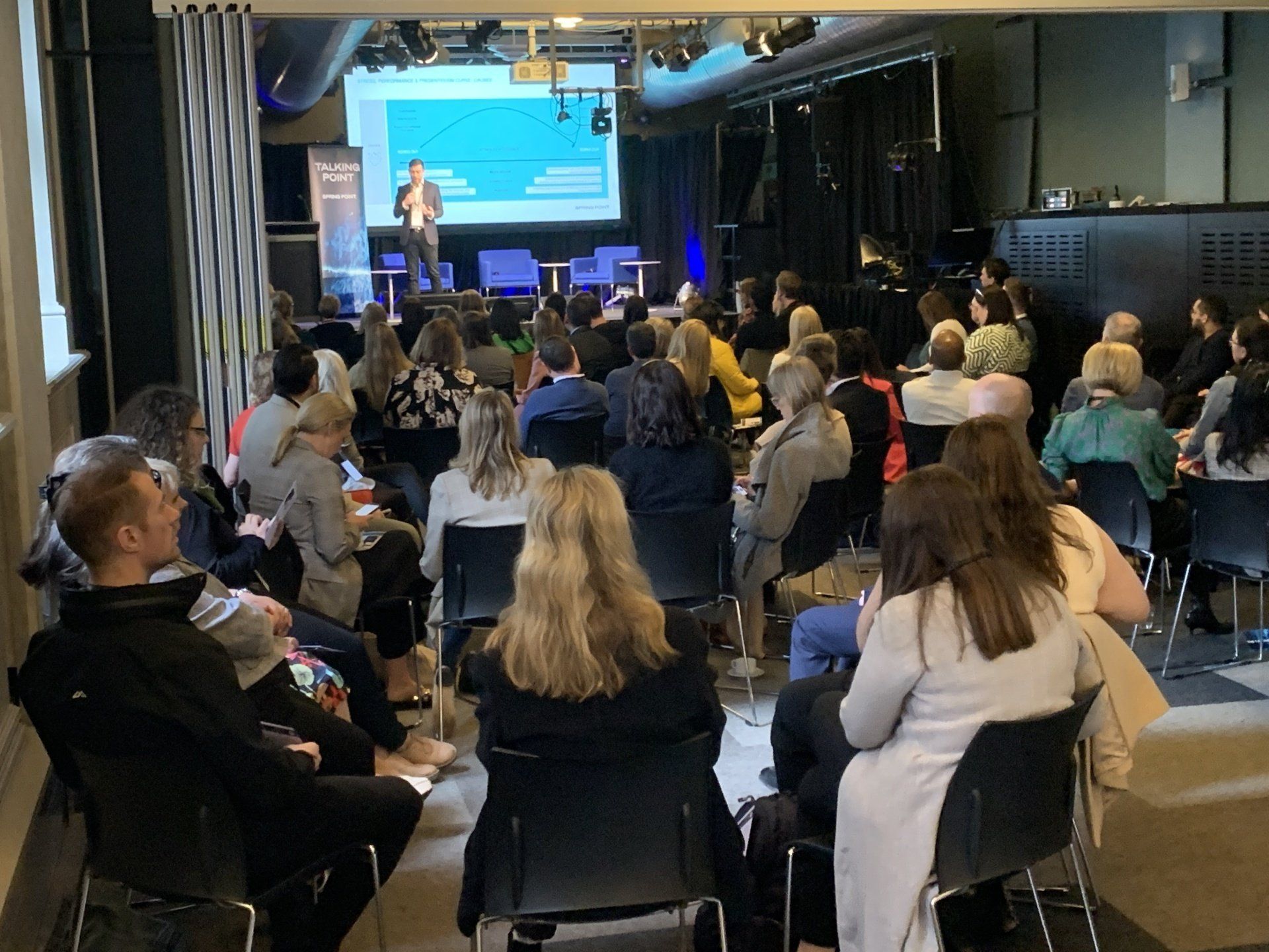 A large group of people are sitting in chairs in front of a projector screen.