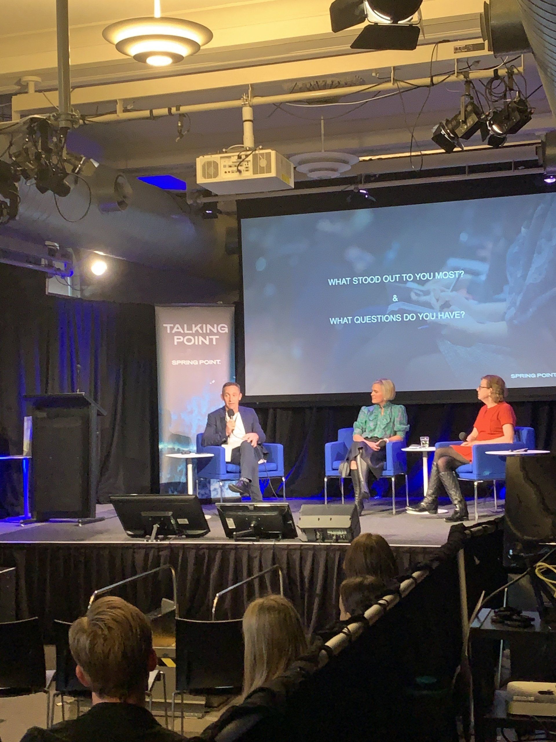 A group of people are sitting on a stage in front of a large screen.
