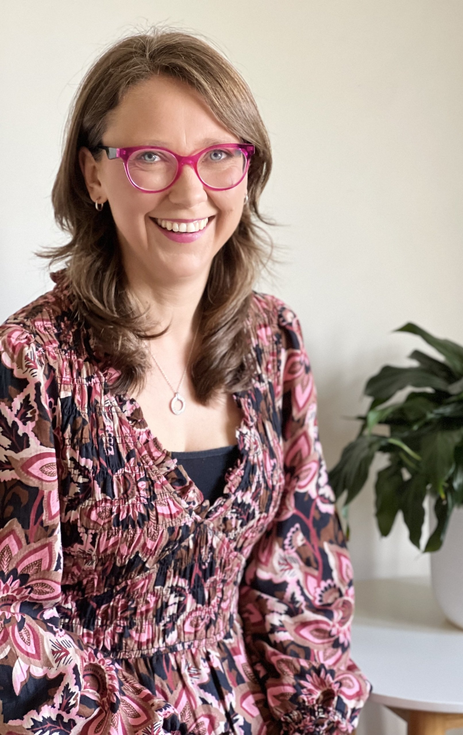 A woman wearing glasses and a floral dress is smiling for the camera.