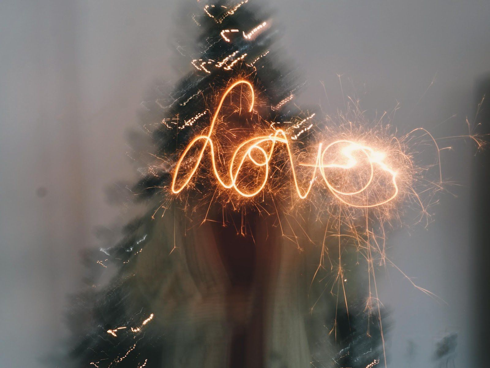 The word love is written with sparklers in front of a christmas tree.