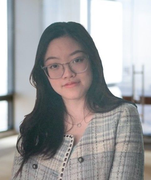A woman is standing in front of a potted plant and smiling.