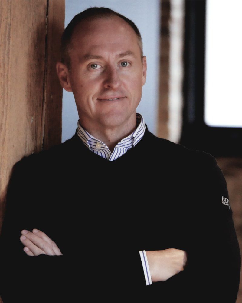 A woman in a brown shirt is leaning against a wall and smiling.
