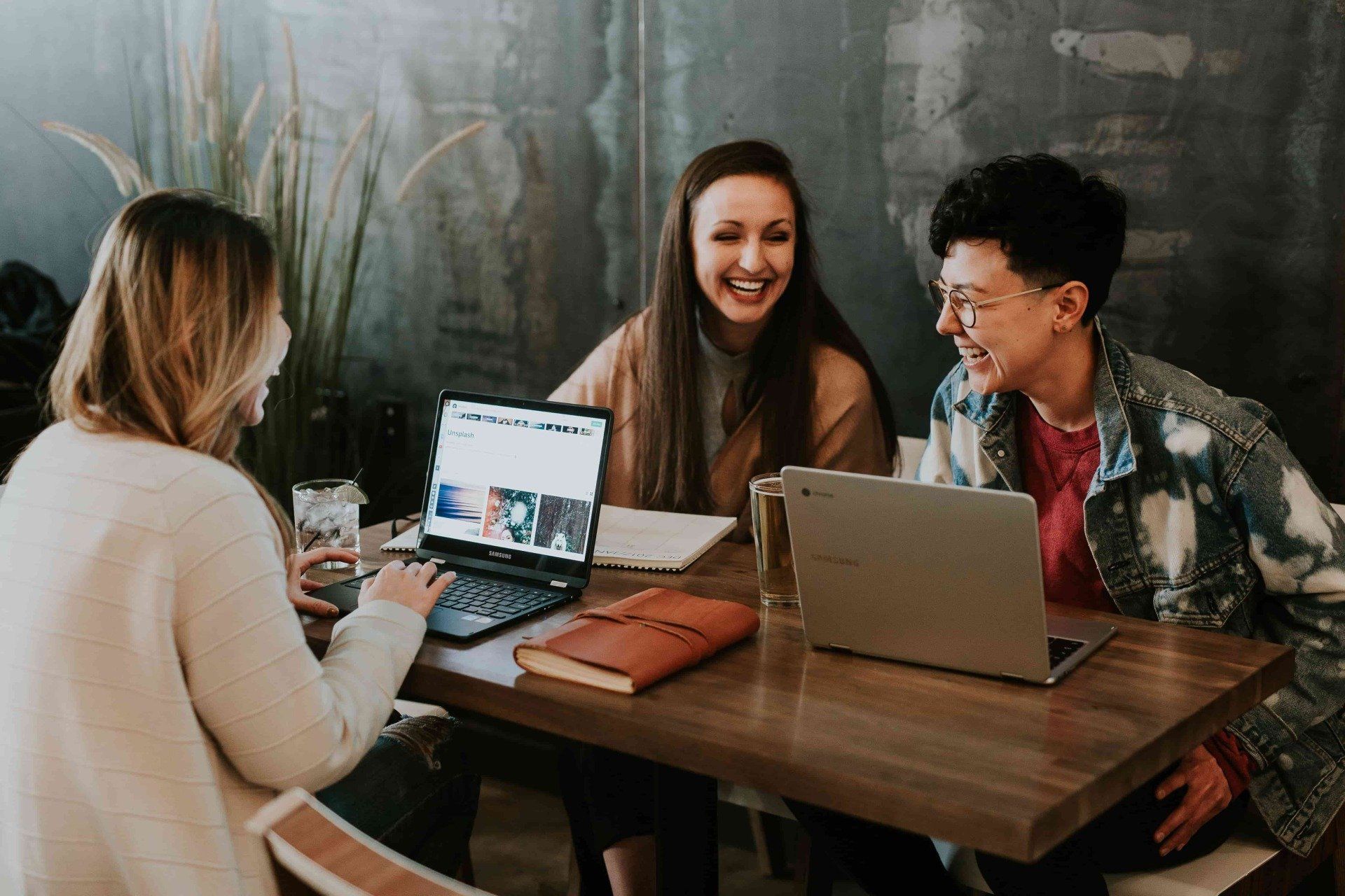 Three women are sitting at a table with laptops.