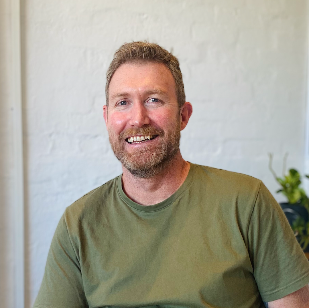 A man with a beard is wearing a green shirt and smiling for the camera.