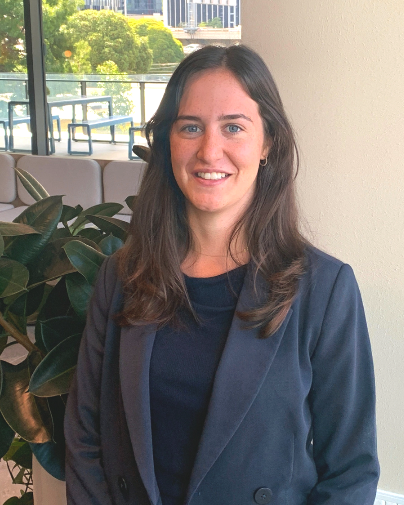 A woman in a suit is smiling for the camera while standing in front of a plant.