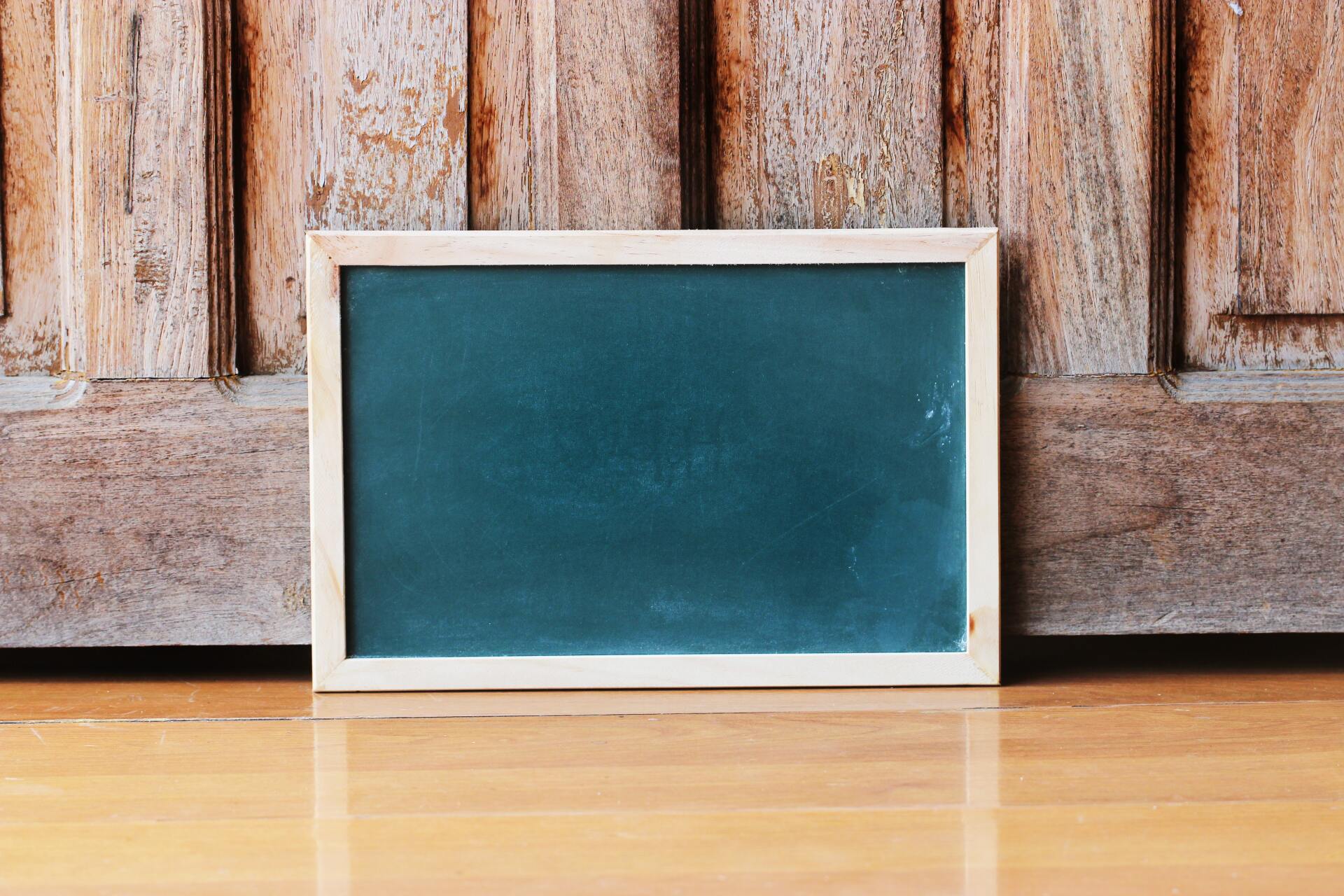 A small square blackboard is sitting on the floor in fron of two large wooden doors