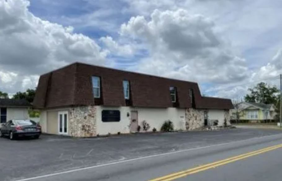 A white building with a brown roof and a car parked in front of it.