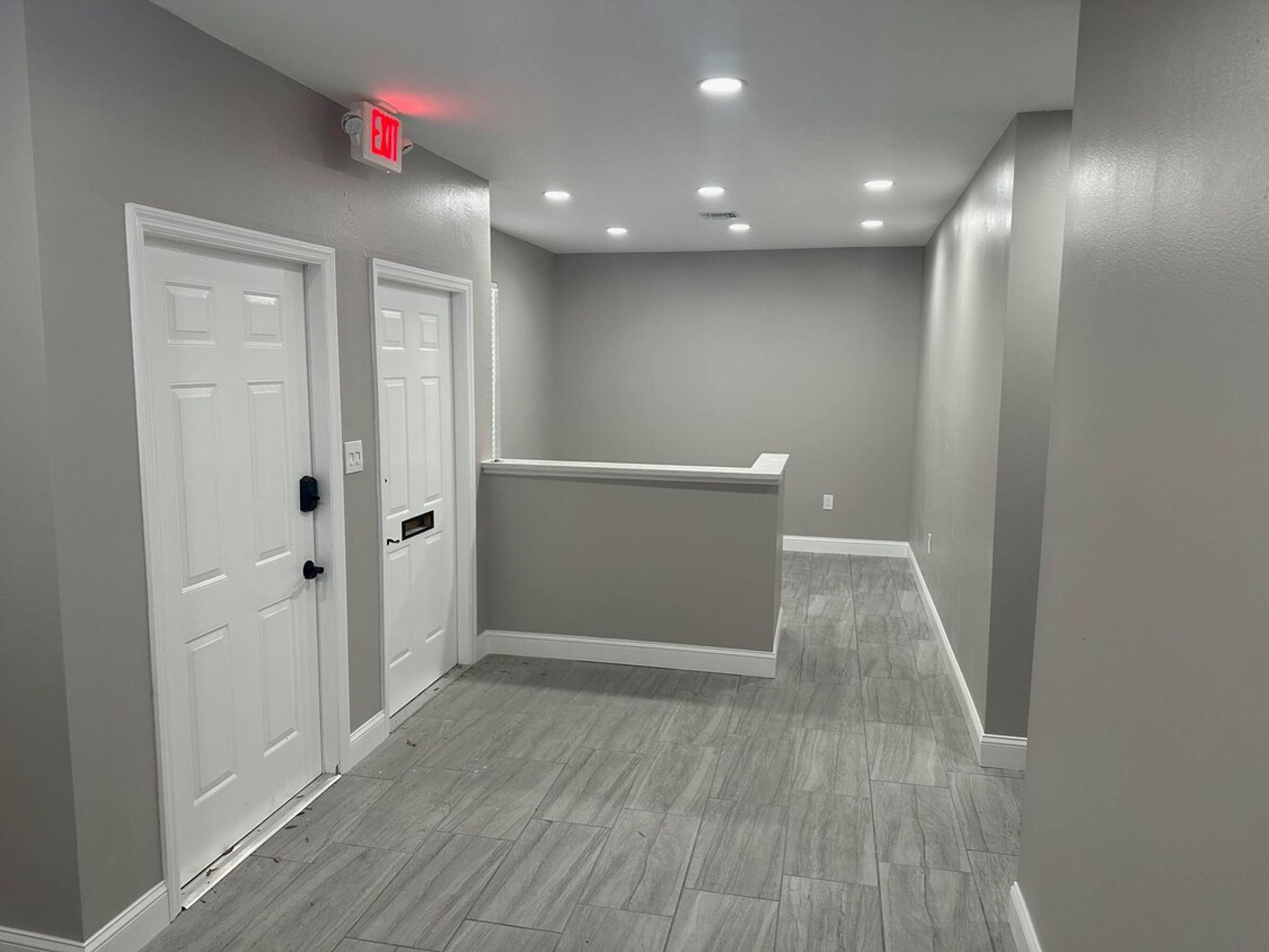 A long hallway with a red exit sign on the ceiling.