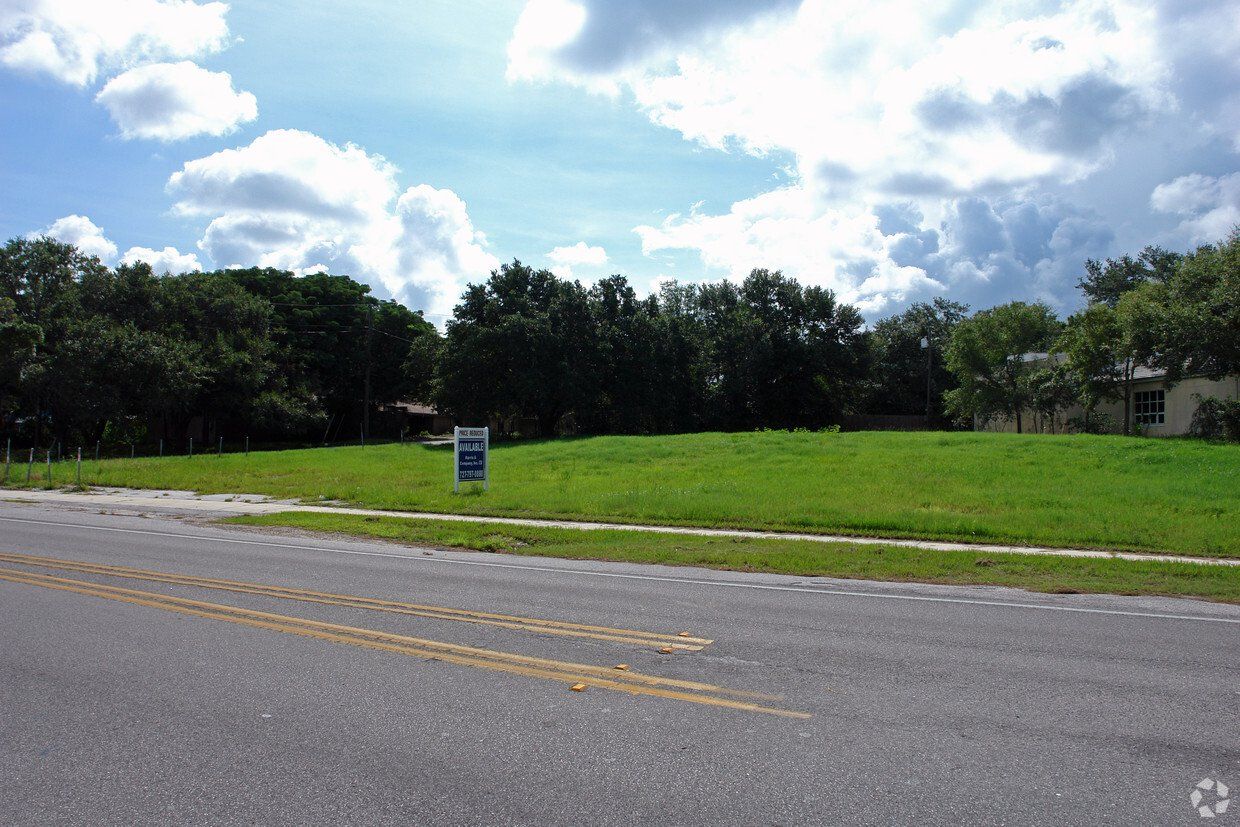 A large grassy field with a for sale sign on the side of the road