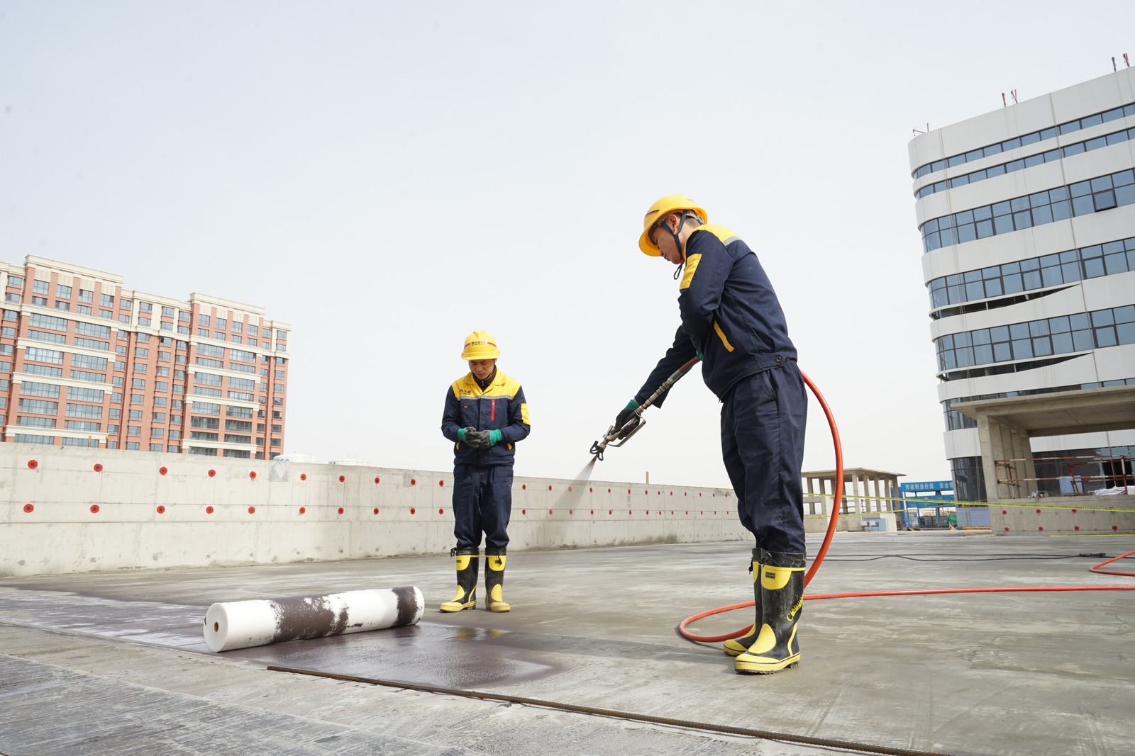 Worker rolling black roofing material across a blue roof surface