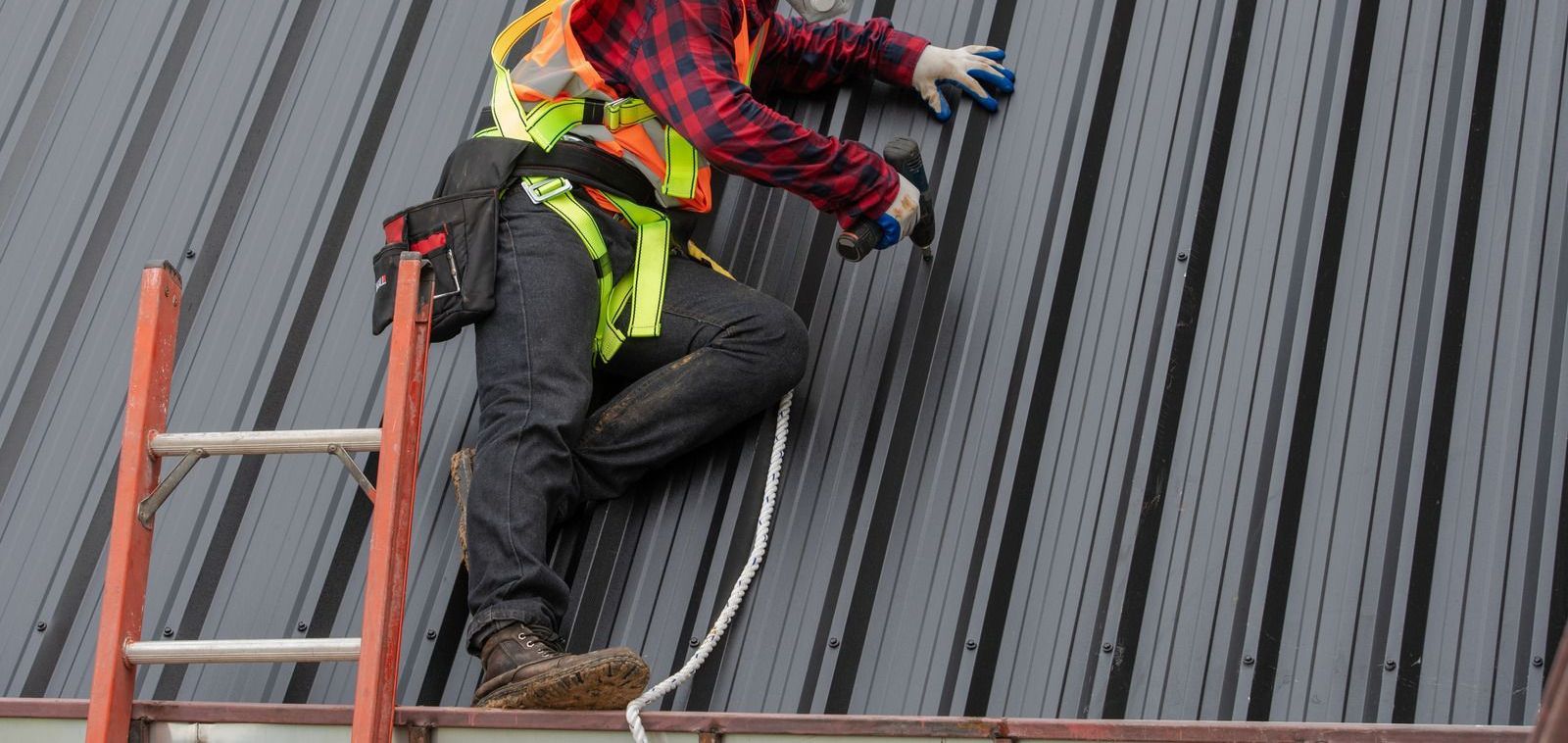 A man is climbing a ladder on top of a metal roof.