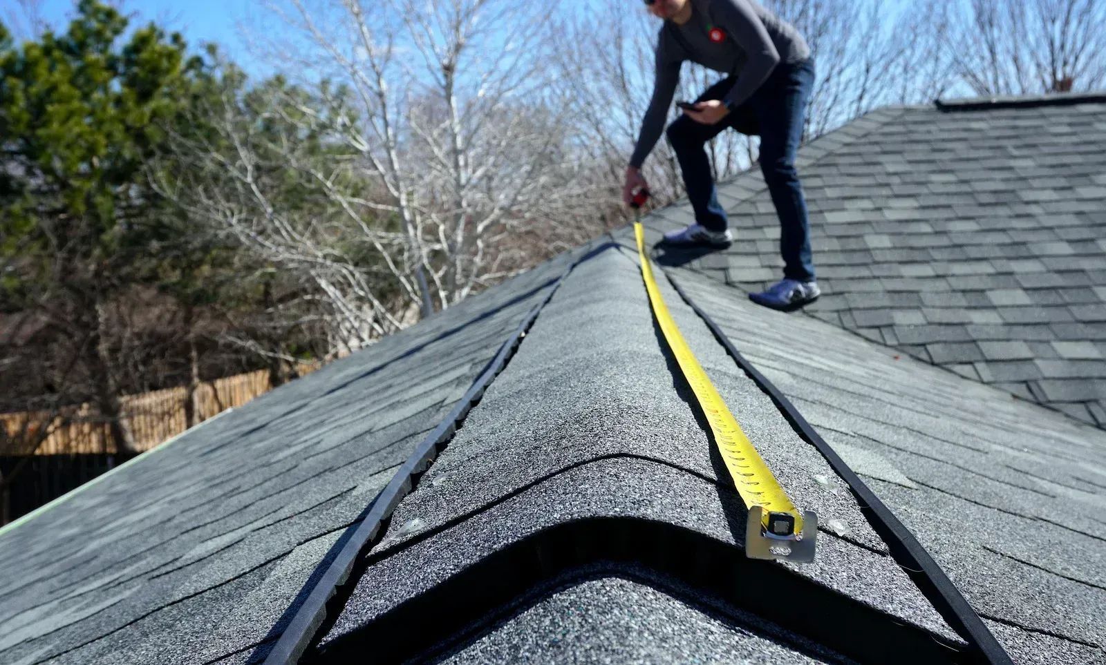 A man is measuring a roof with a tape measure.