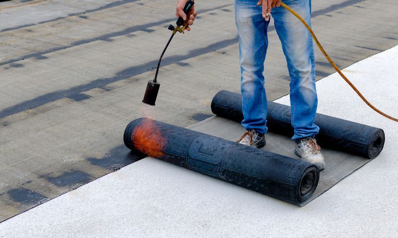 A man is using a torch on a roll of roofing material.