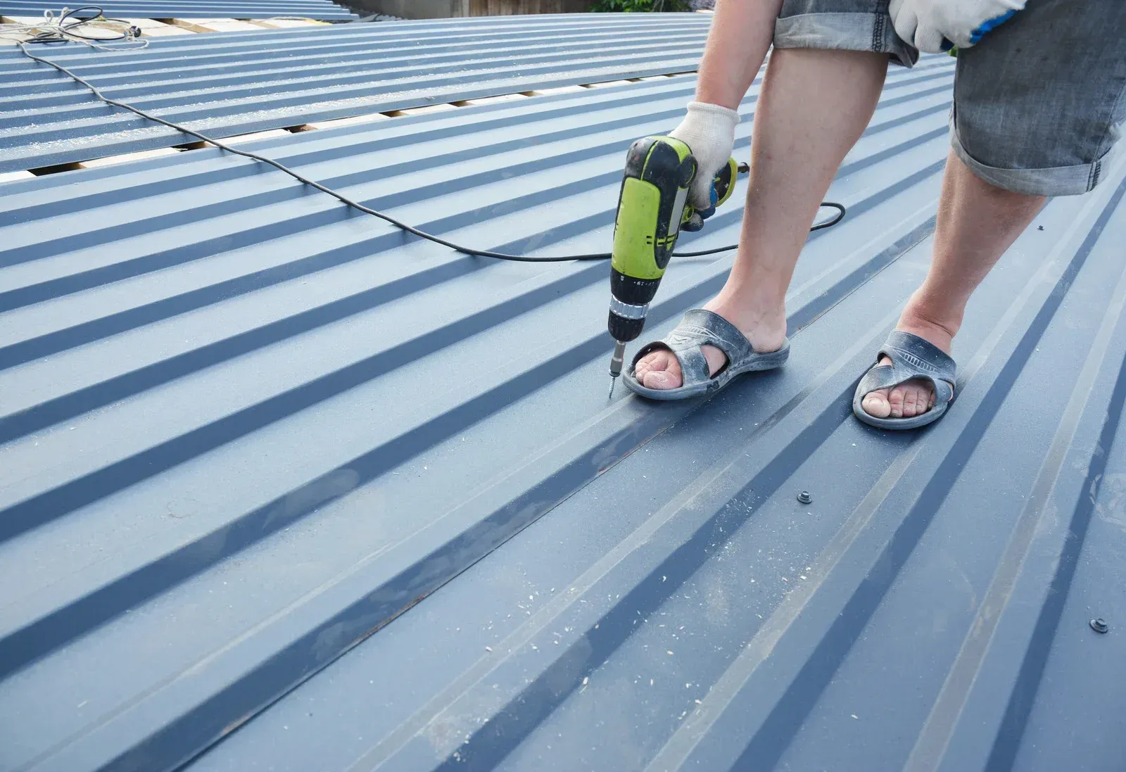 Person in sandals using a drill on a corrugated metal roof.