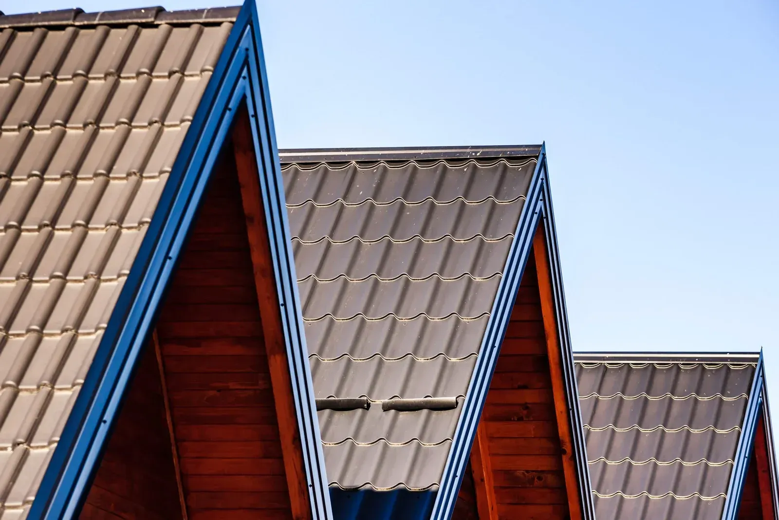 Three brown roof peaks with dark gray tiles against a clear blue sky.
