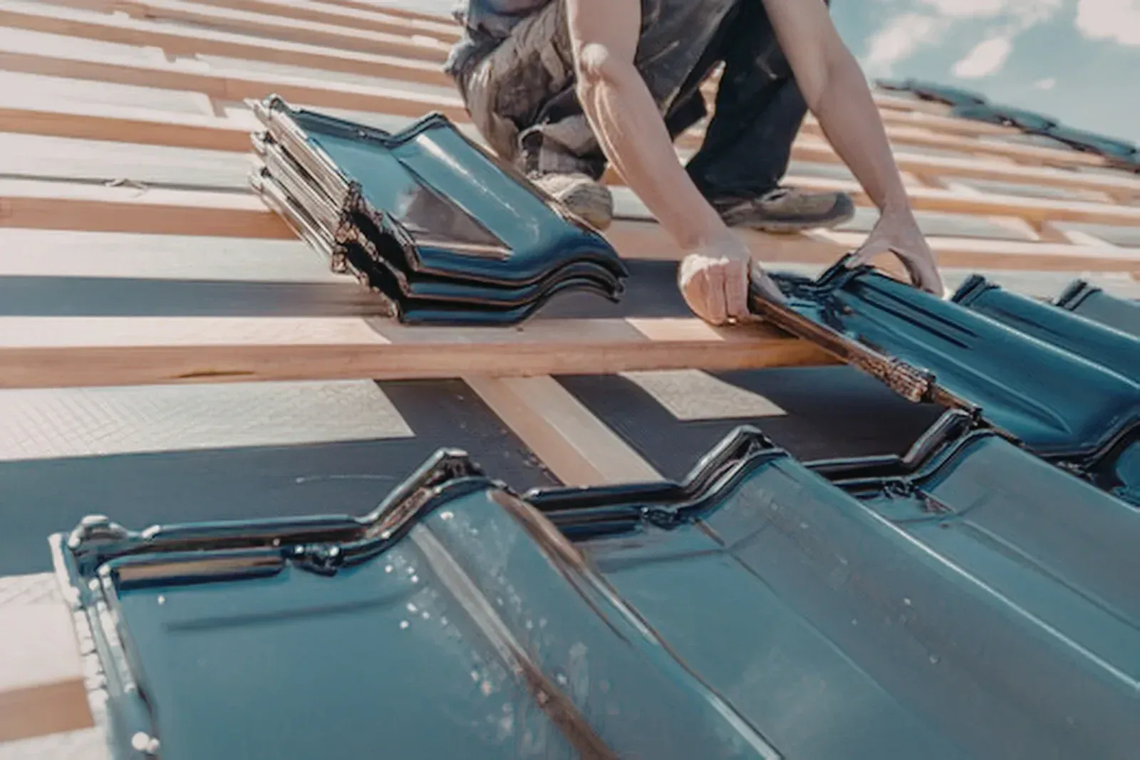 Person installing blue roof tiles on a sloped roof with wooden battens