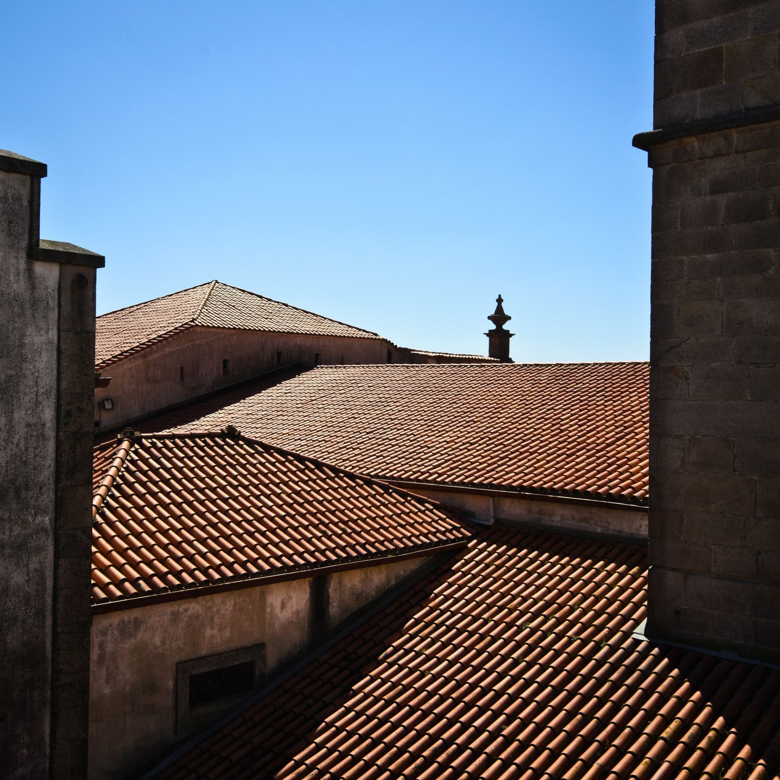 Clay tile rooftops under a clear blue sky, viewed from between buildings.