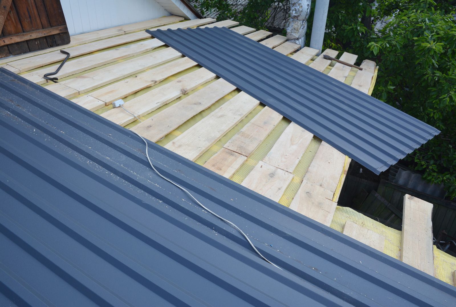 Blue corrugated metal roofing sheets partially installed over exposed wooden roof framing