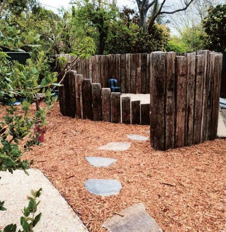 Circular wooden fence encloses a small garden seating area with stepping stones.