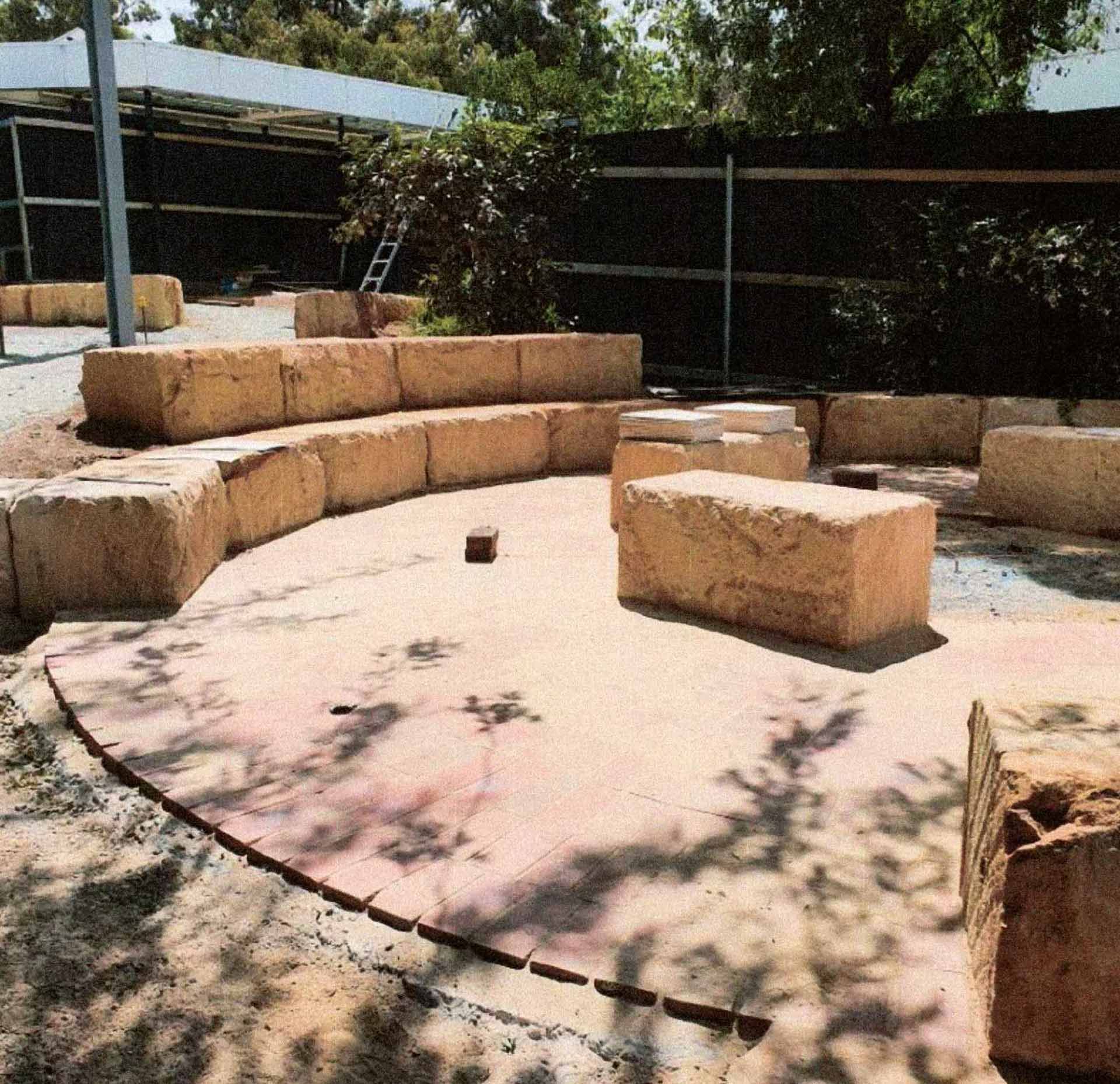 Park landscaping with rows of plants in red mulch, trees, and blue sky.