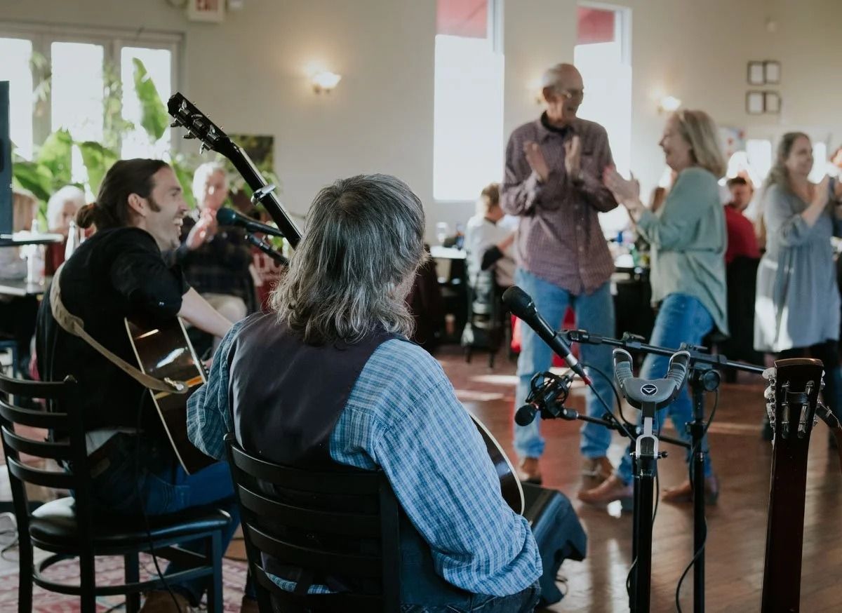 Acoustic band playing; people clapping and dancing in a well-lit room.