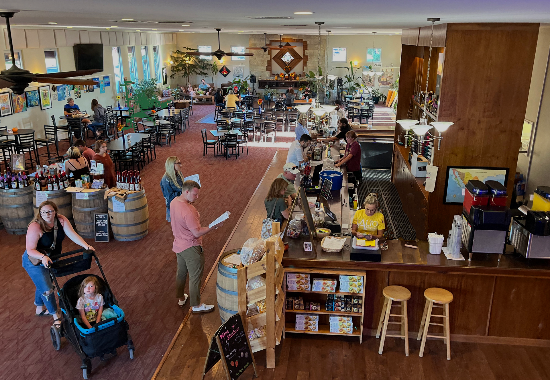 Large, busy restaurant with patrons. A family with a stroller near entrance, bar with stools.